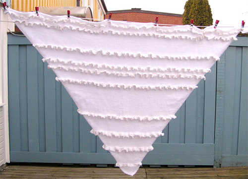 Sltstickad vit trekantsjal med vita glansiga volanger.