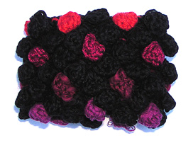 Rtstickat svart armband med moucher i olika cerise-rda frger och svart.